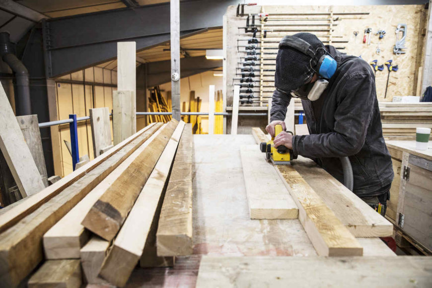 mężczyzna używający szlifierki taśmowej do szlifowania desek